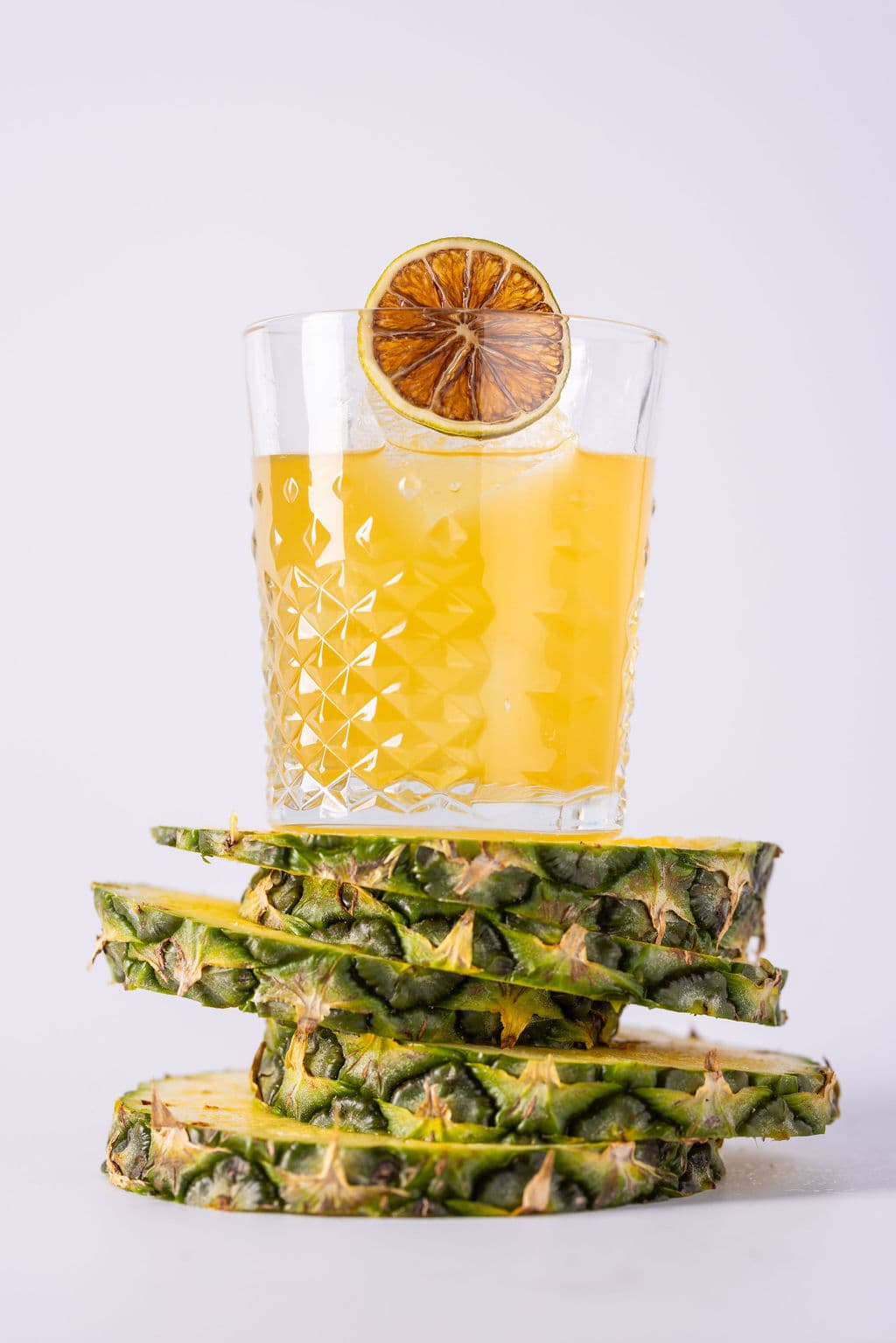 A yellow cocktail with a dried lime wheel on a stack of pineapple slices