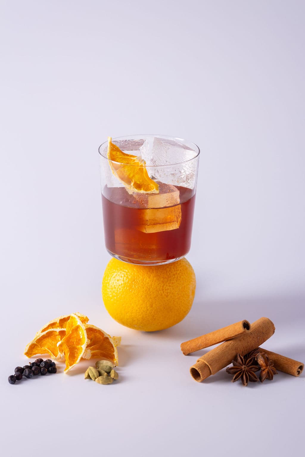 A Negroni balanced on an orange, surrounded by dried orange, cinnamon sticks and star anise